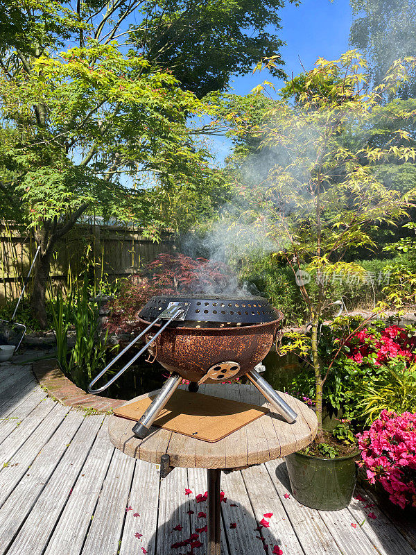 生锈的水壶烧烤用室外作为火坑/木材燃烧器，在后花园燃烧木材时吸烟，关注前景